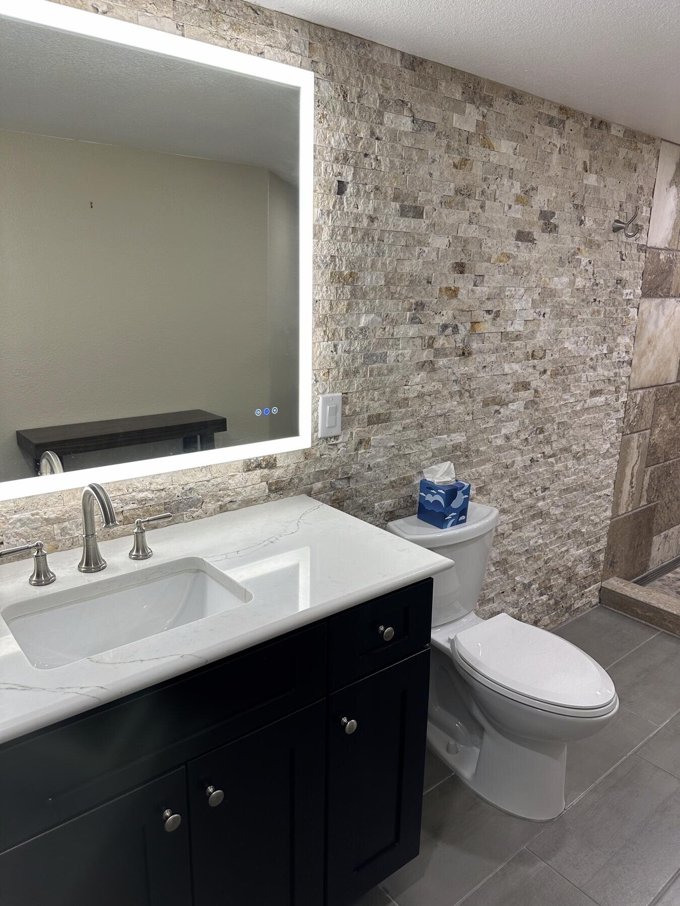Finished bathroom black vanity with a backlit mirror, viewed toward the toilet area, completed remodel by The Build Squad