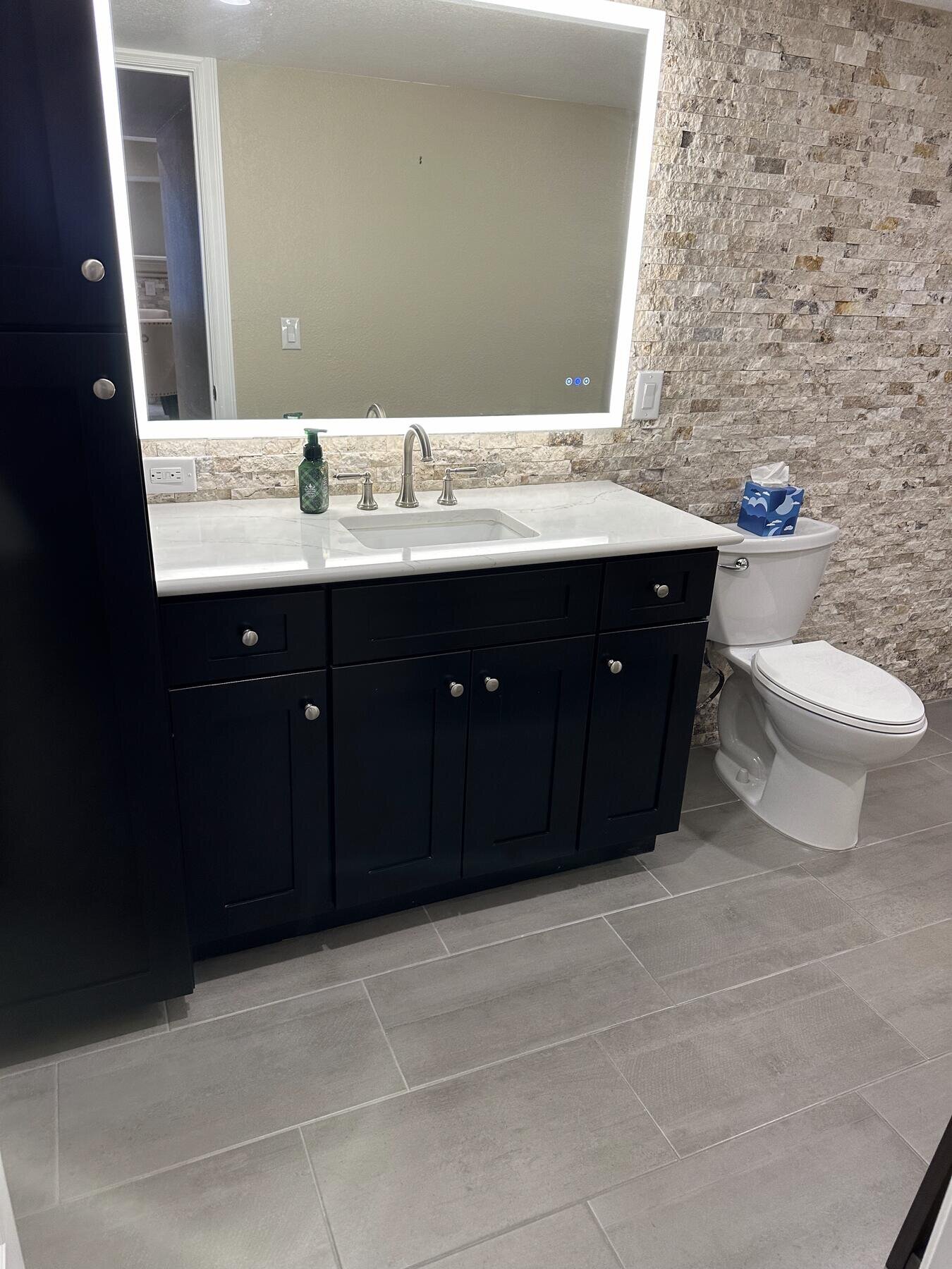Finished bathroom with a matte black vanity and stacked-stone accent wall, completed remodel by The Build Squad