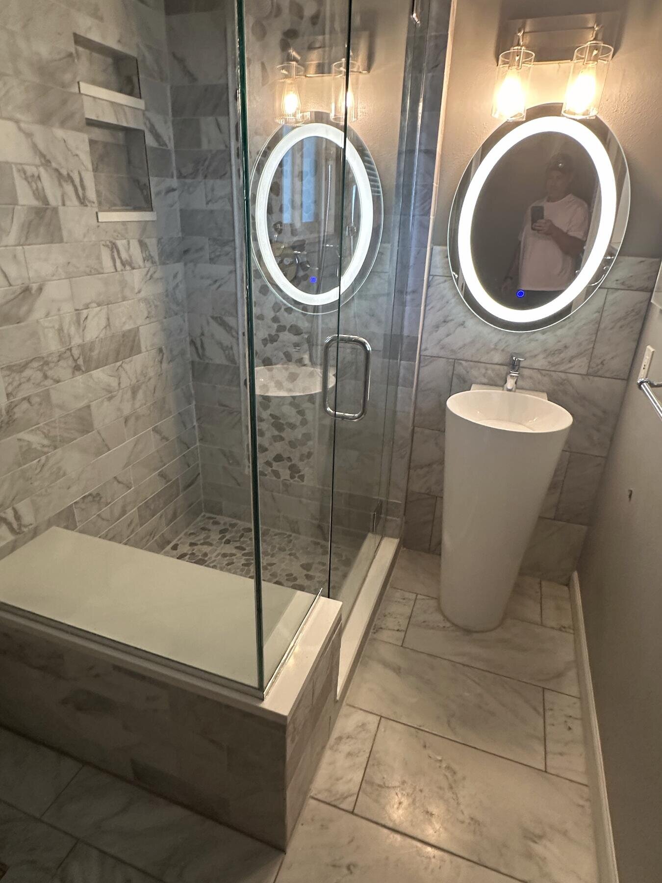 Finished bathroom with a dual-sink vanity, backlit oval mirrors, and glass shower enclosure, completed remodel by The Build Squad