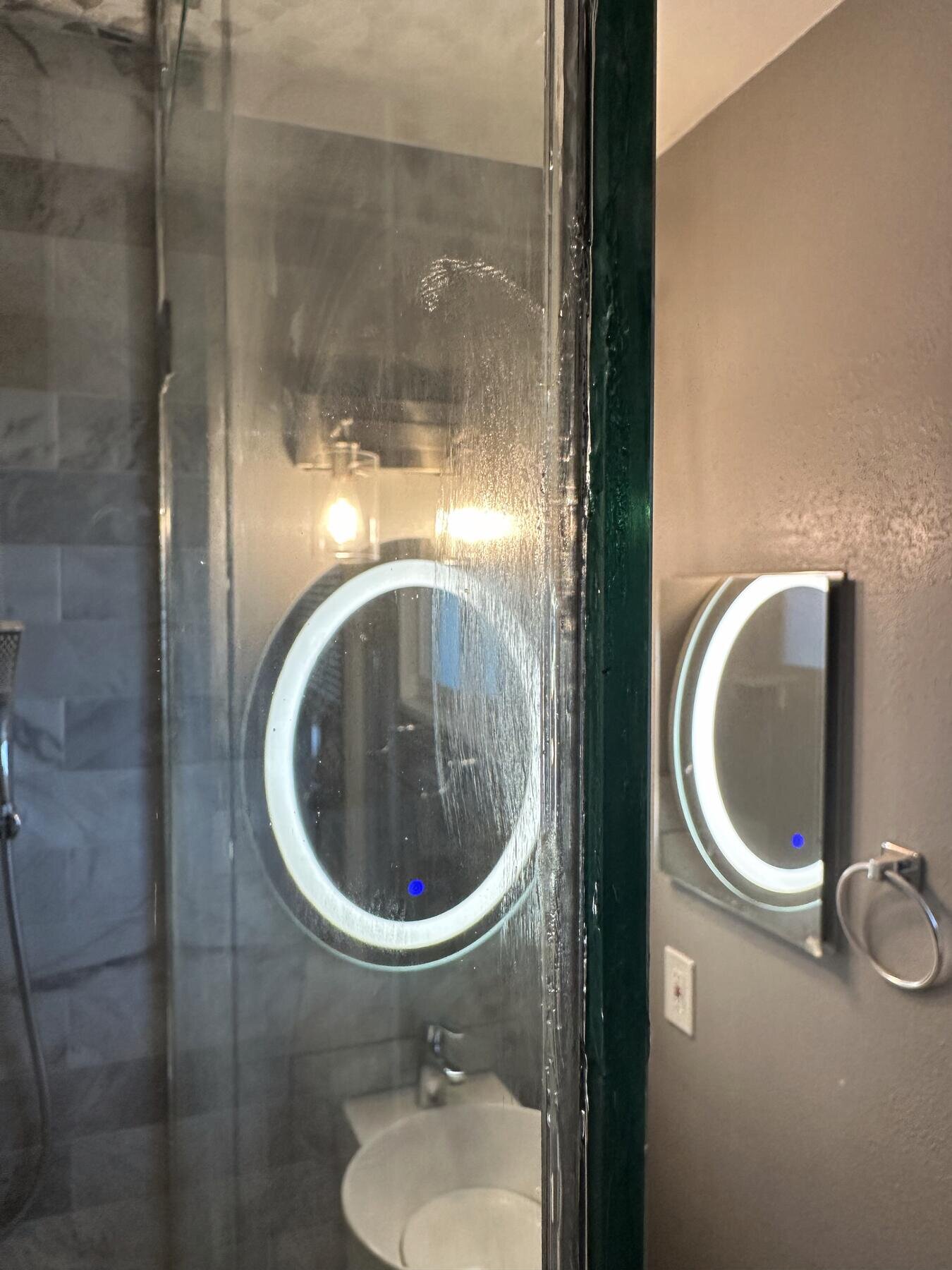 Finished bathroom dual vanity with backlit mirrors and a glass shower entry, completed remodel by The Build Squad