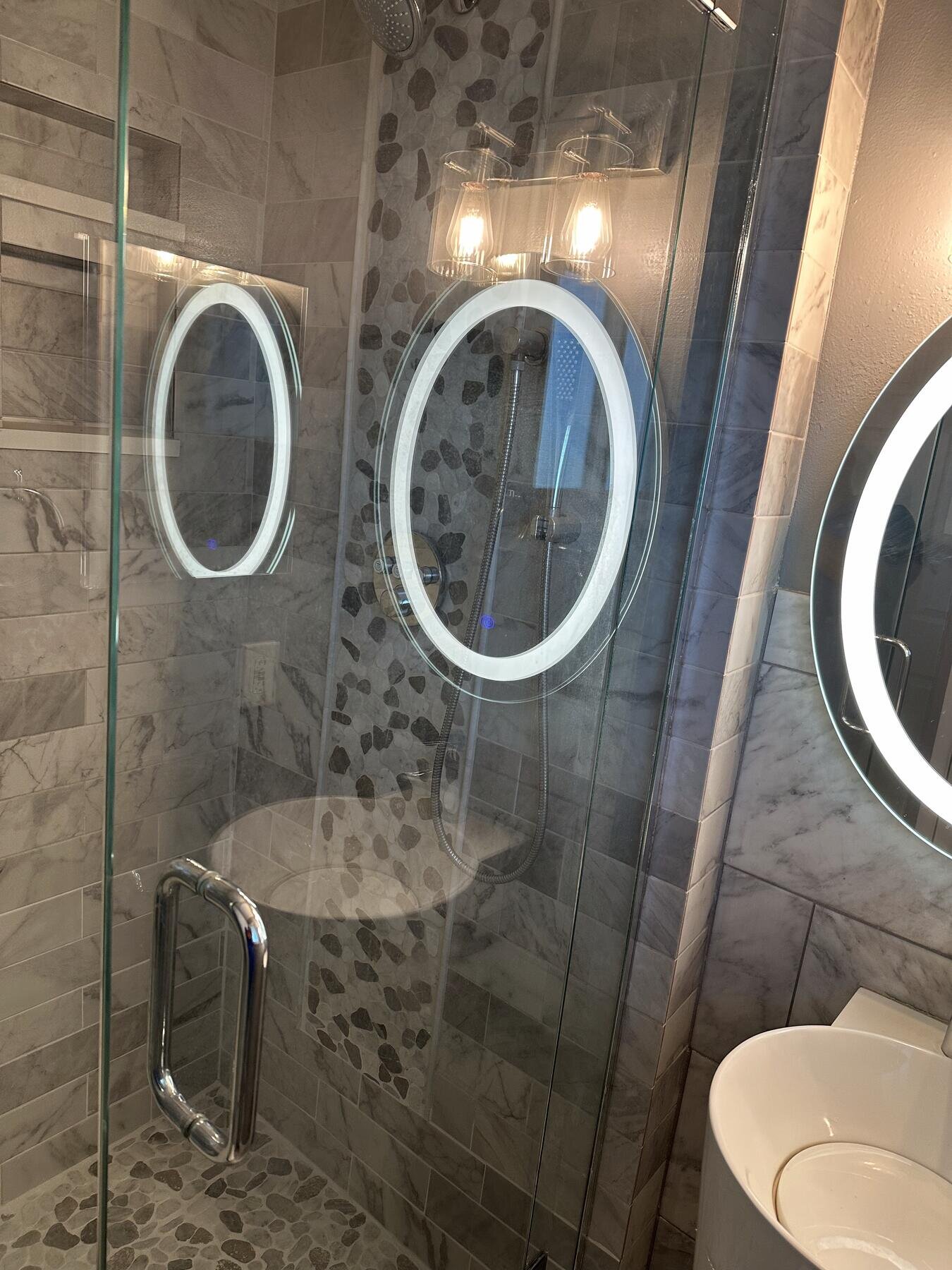 Finished bathroom with a glass-enclosed shower and dual backlit oval mirrors, completed remodel by The Build Squad