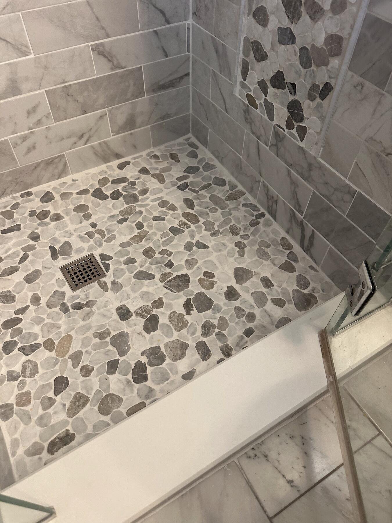 Finished shower with a pebble-tile floor and built-in bench, completed bathroom remodel by The Build Squad