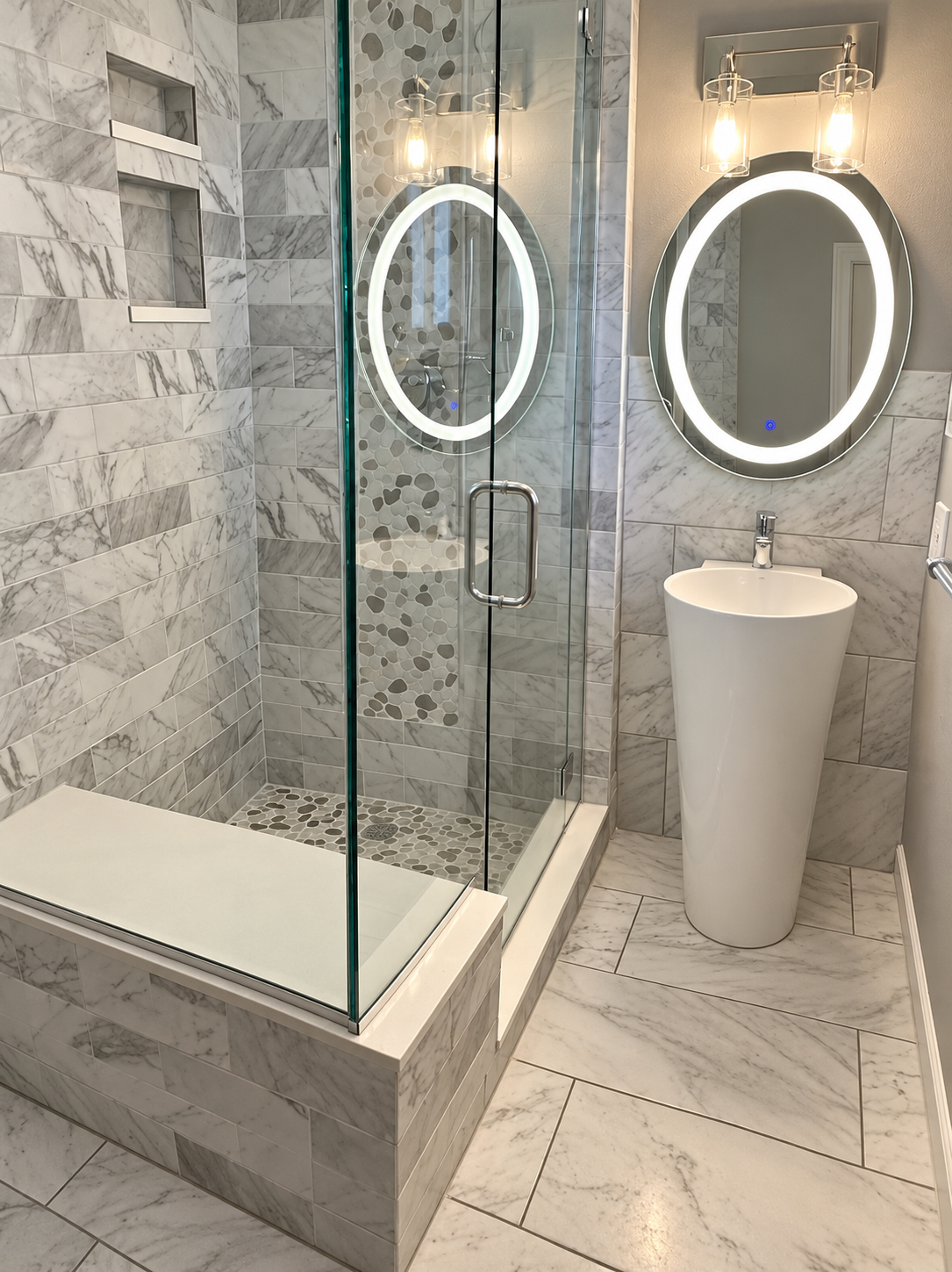 Marble tile shower and pedestal sink with round backlit mirrors