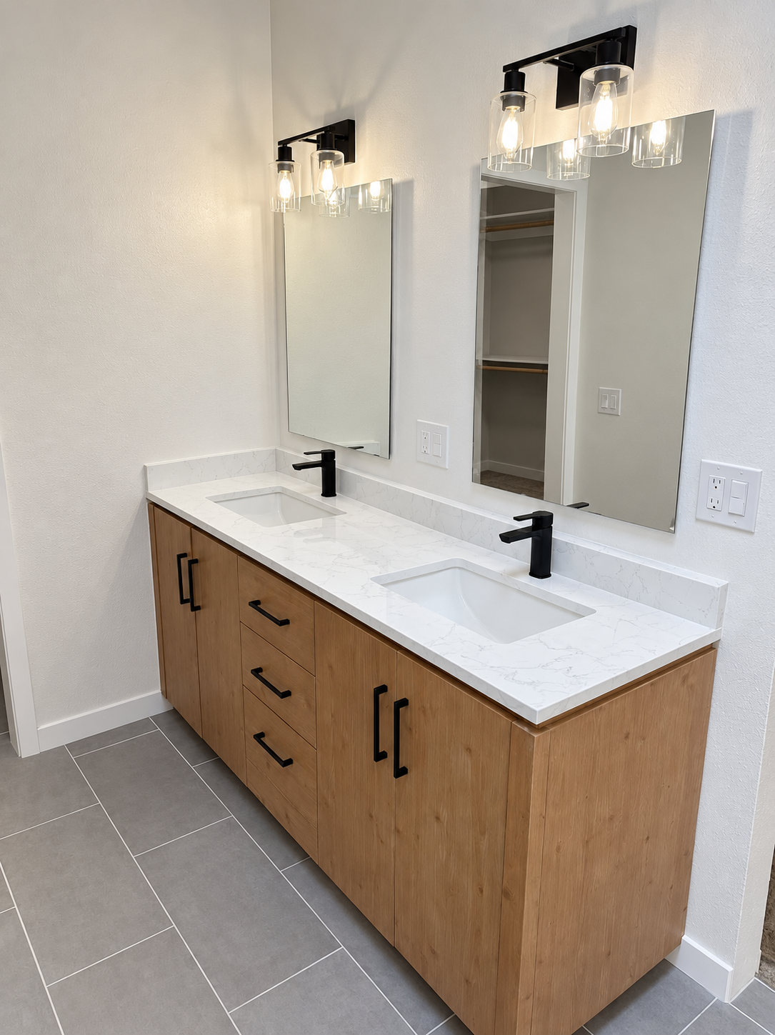 Modern double vanity with wood cabinetry, black hardware, and framed mirrors