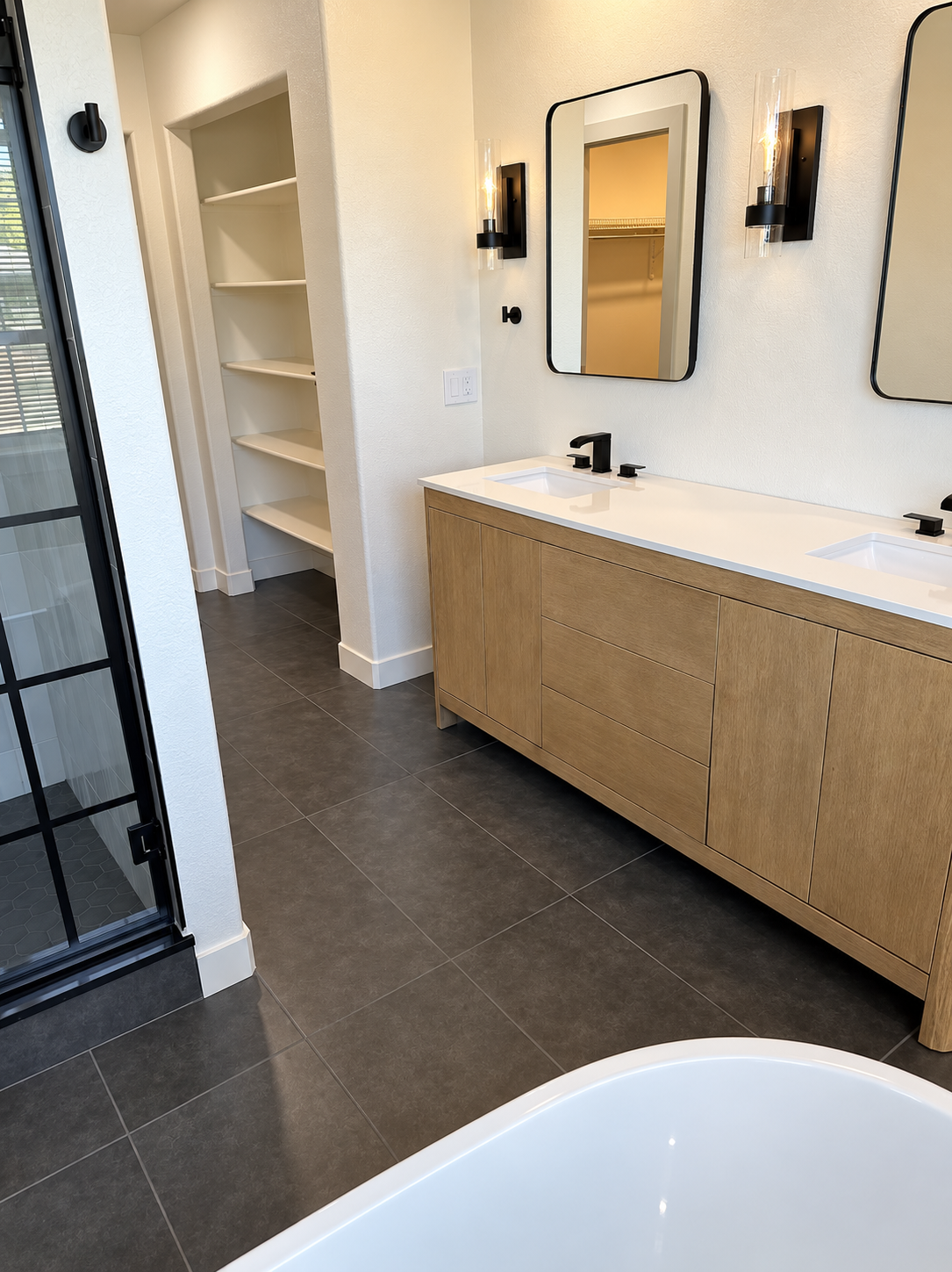 Bathroom with wood vanity, black fixtures, and freestanding tub, angled view