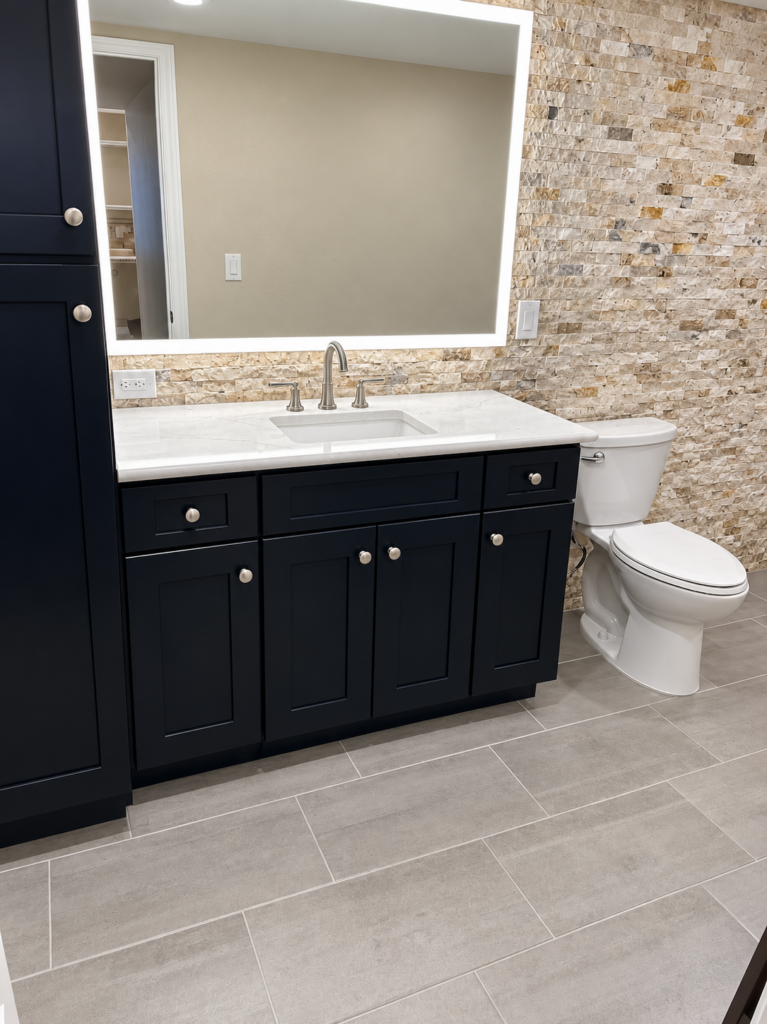 Navy vanity and stacked-stone accent wall in a bathroom, wide view