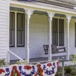 Front view of a white house in Texas with a porch swing and flags hanging