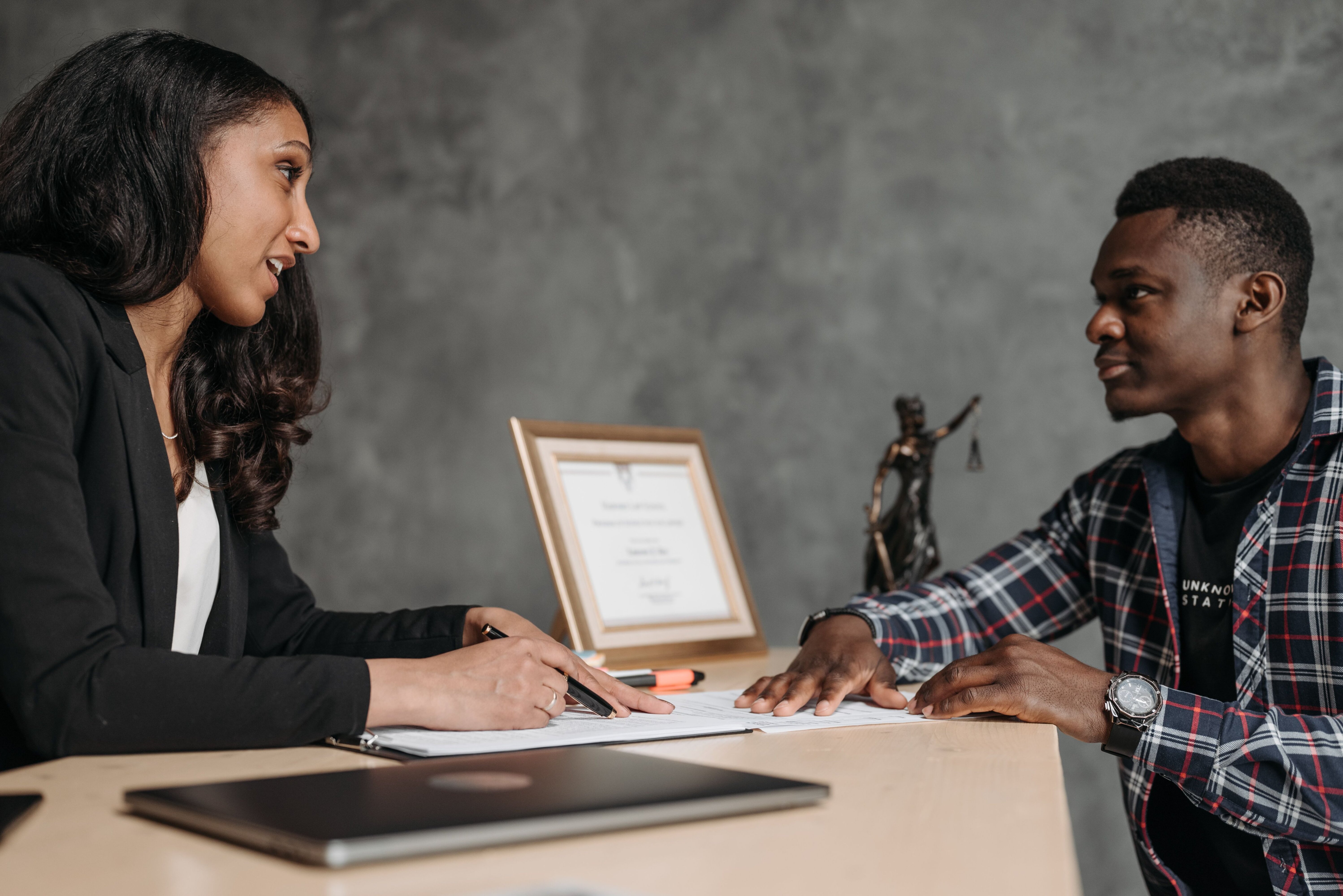 A homeowner consulting with an attorney at a desk, representing deciding whether to hire a foreclosure attorney