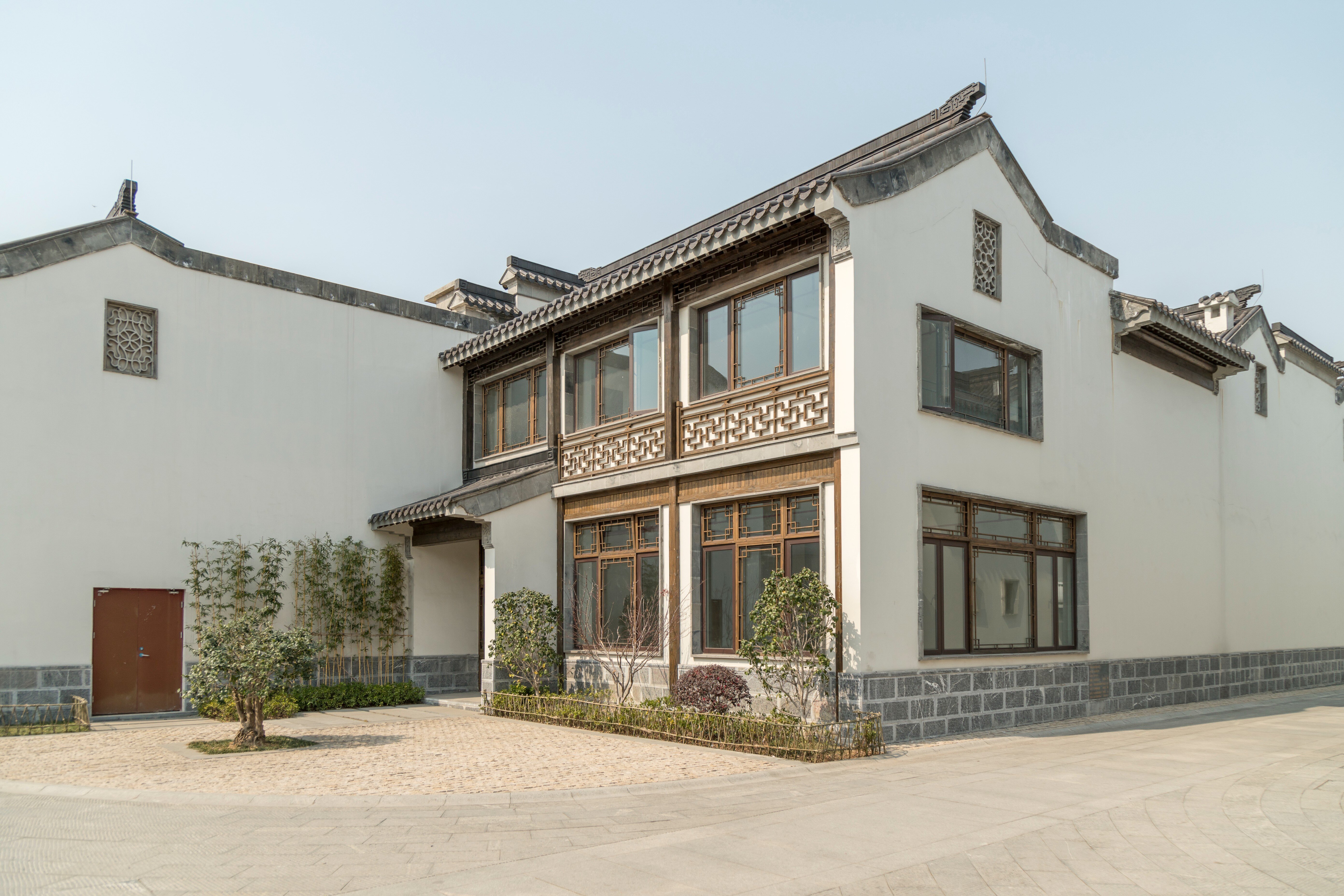 Traditional two-story house with white walls, decorative architecture, large windows, and a paved courtyard.