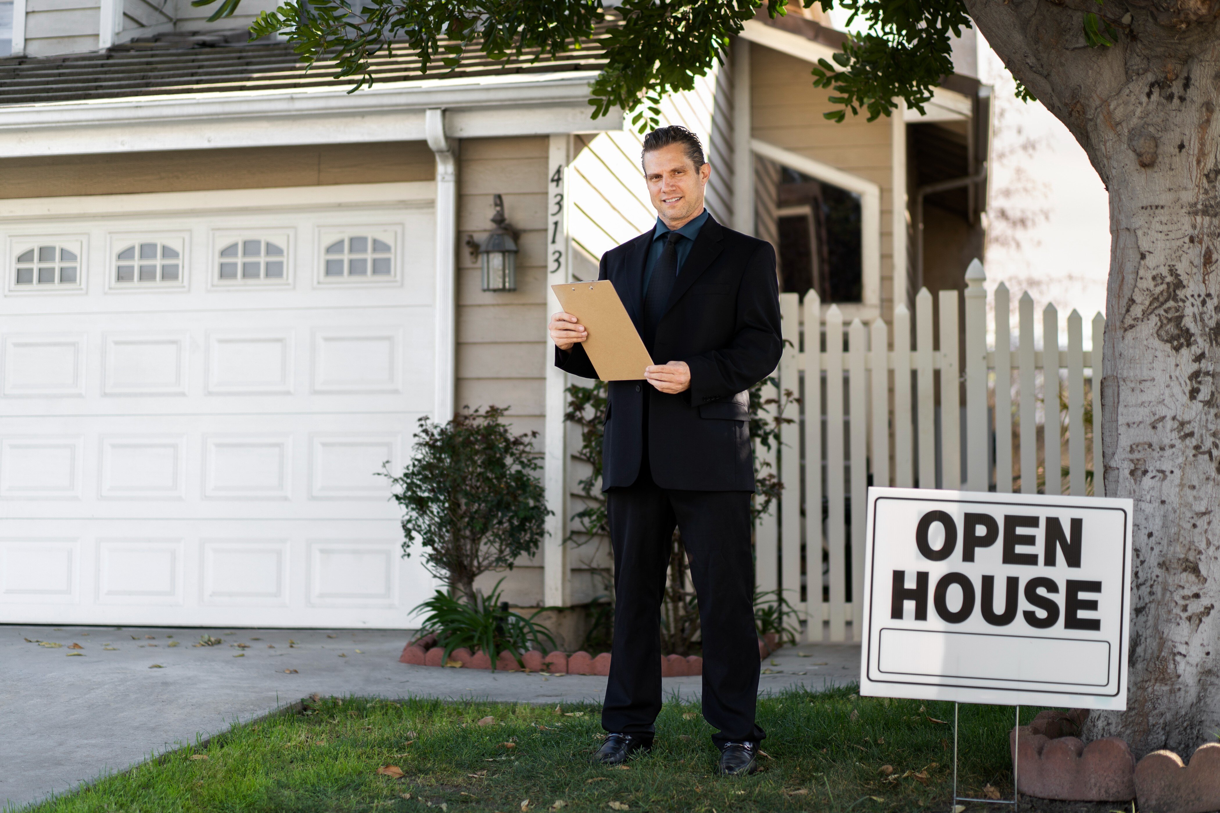 Real estate agent standing outside a house with an open house sign, representing a home sale.