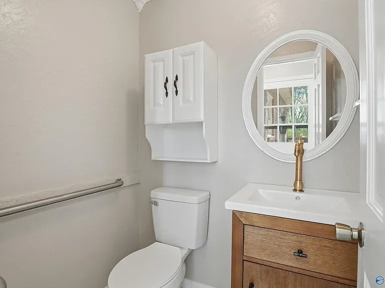 Completed small powder room remodel featuring a wooden vanity with a white vessel sink, a brushed gold faucet, a round mirror, and a white medicine cabinet.