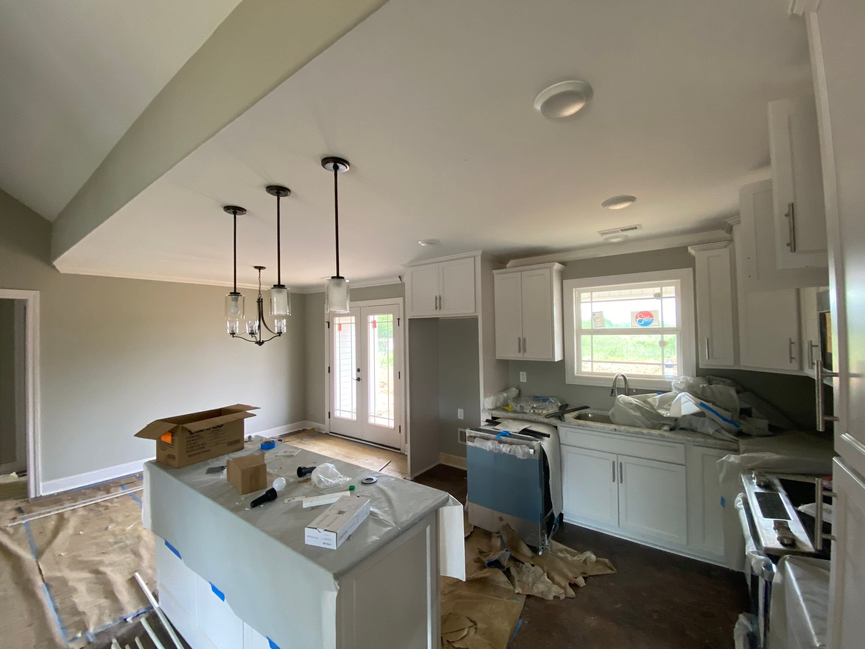 Custom kitchen under construction featuring white shaker cabinets, a central kitchen island with modern glass pendant lights, and stainless steel appliances.