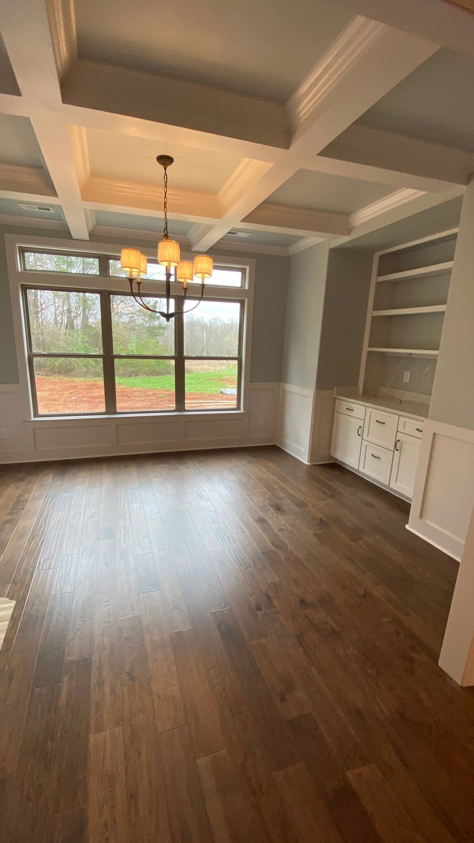 Custom residential millwork installation including a white built-in hutch, coffered ceiling beams, and professional hardwood floor finishing by local home remodeling contractors in Huntsville, Alabama