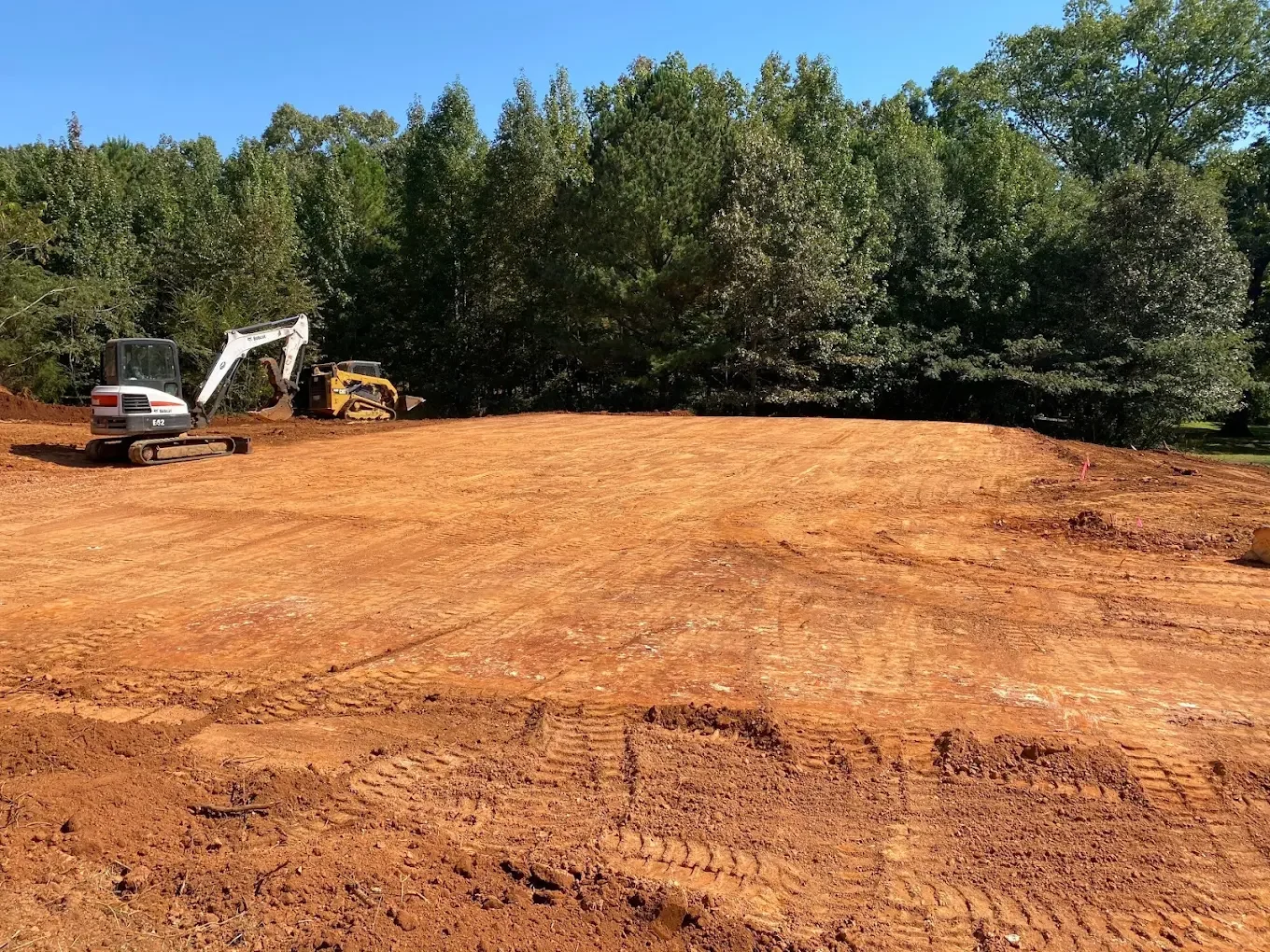 Cleared residential construction site with graded foundation pad and excavation equipment preparing for a new custom home build.
