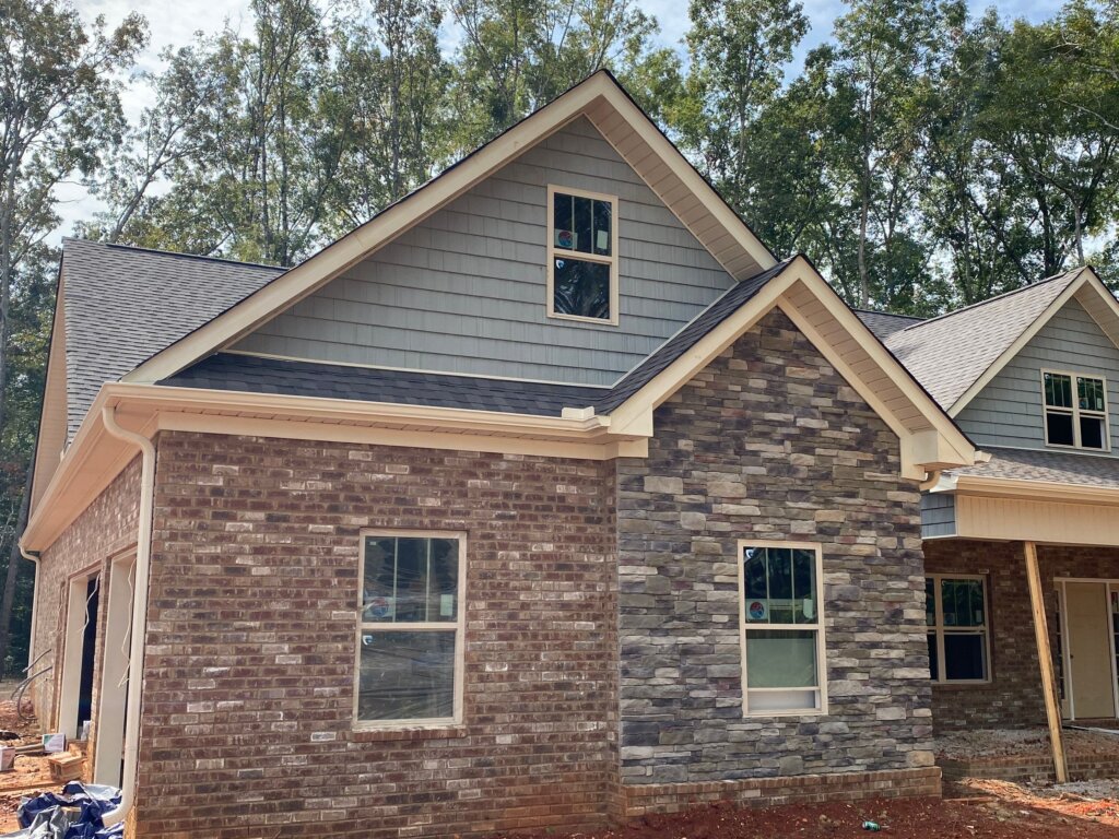 New residential home exterior featuring a combination of red brick, gray stacked stone veneer, and gray shake siding accents on a multi-gabled roofline.