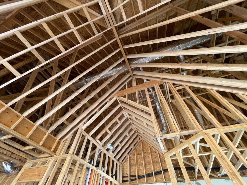 Detailed interior construction shot looking up at complex dimensional lumber roof framing, ridge boards, and ceiling supports.