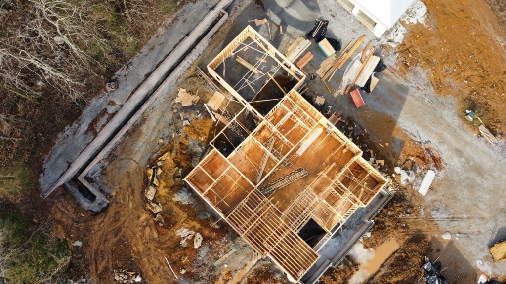 Construction phase of a modern farmhouse featuring exposed timber framing, large square wooden support columns.