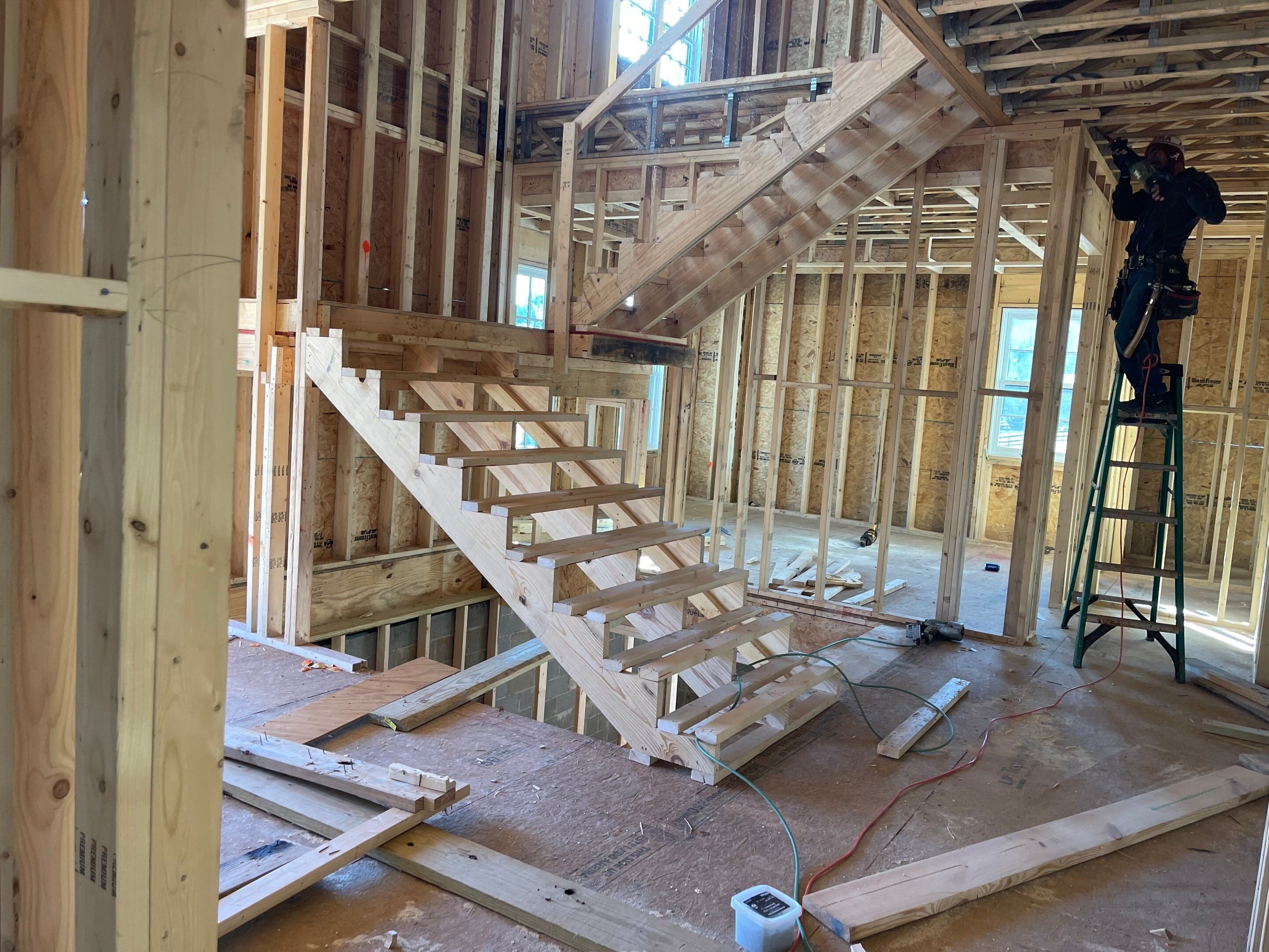 Custom residential house construction site showing the rough framing phase of a double-turn wooden staircase with exposed stair stringers and wood wall studs.