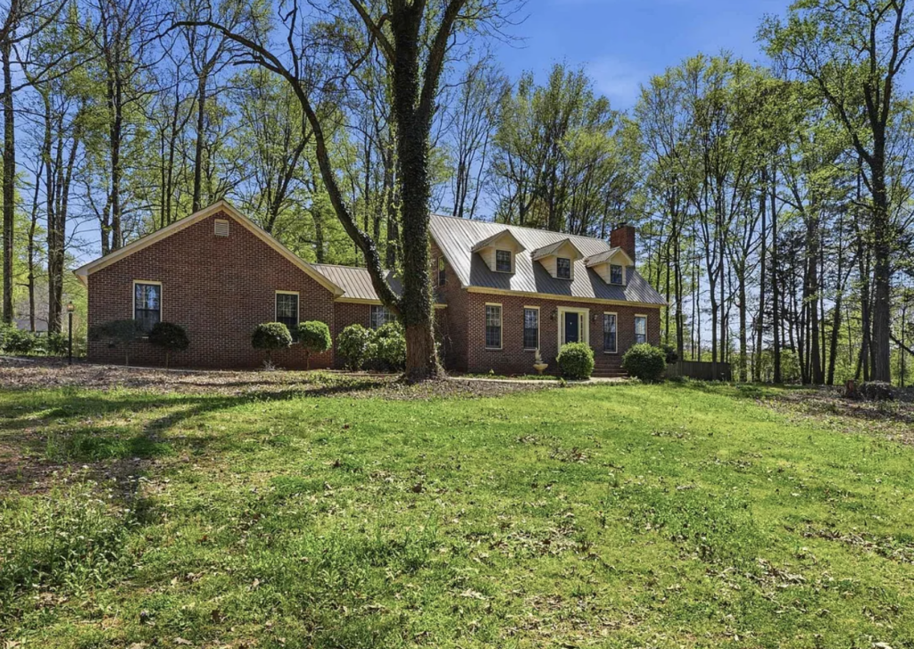 One-story red brick house featuring a newly installed bronze standing seam metal roof, three roof dormers, and a brick chimney.