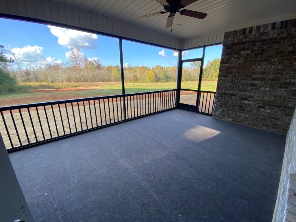 Large screened-in porch with a concrete floor, black railings, a ceiling fan, and a brick accent wall looking out onto a large backyard field.