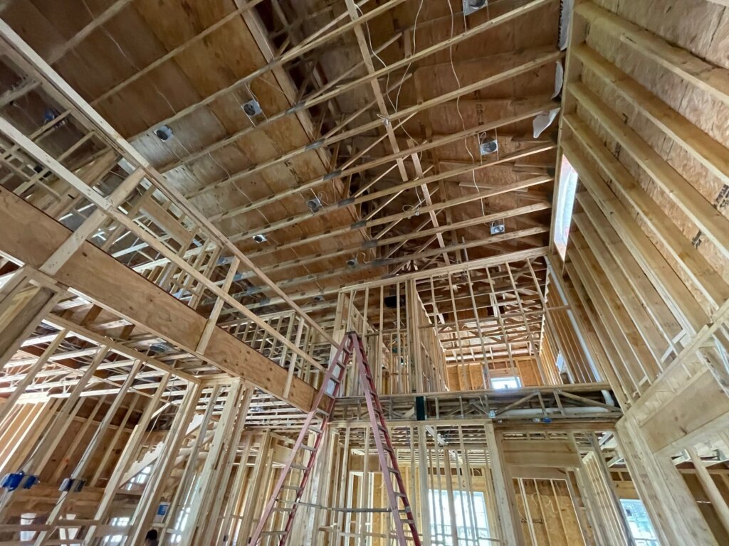Wood framing of a custom home under construction with exposed roof trusses, second-story framing, and open floor plan.