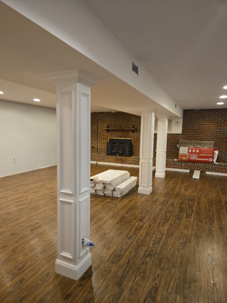 Finished basement remodel featuring luxury vinyl plank flooring, decorative columns, exposed brick fireplace, and an open entertainment space in Huntsville, AL.