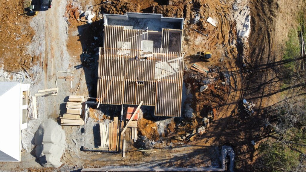 Aerial view of a luxury custom home under construction showing roof framing, foundation, and active job site in Hazel Green, AL.