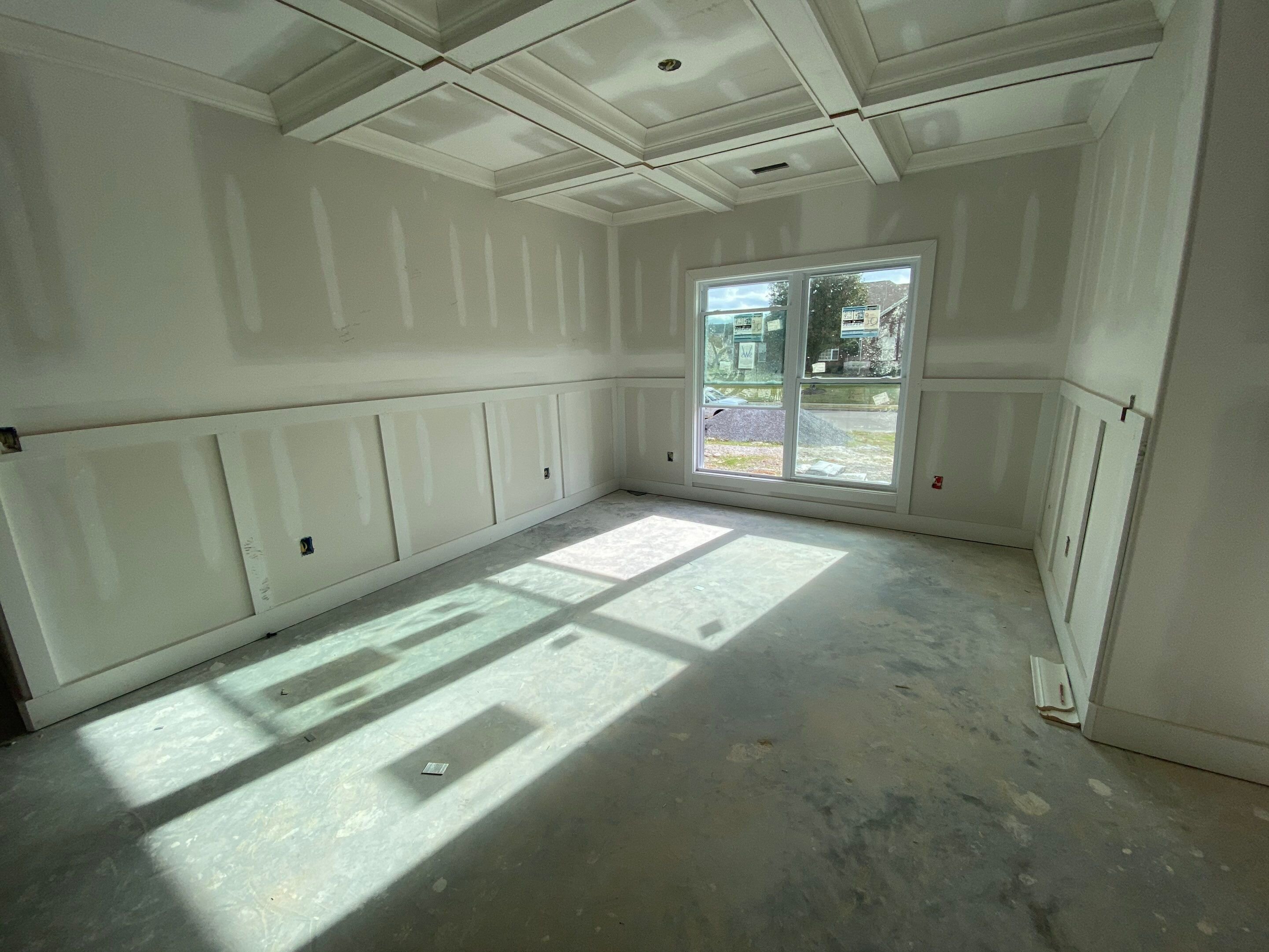 Luxury custom home interior with coffered ceiling, board and batten wall trim, and large picture window during the finishing stage in New Market, AL.