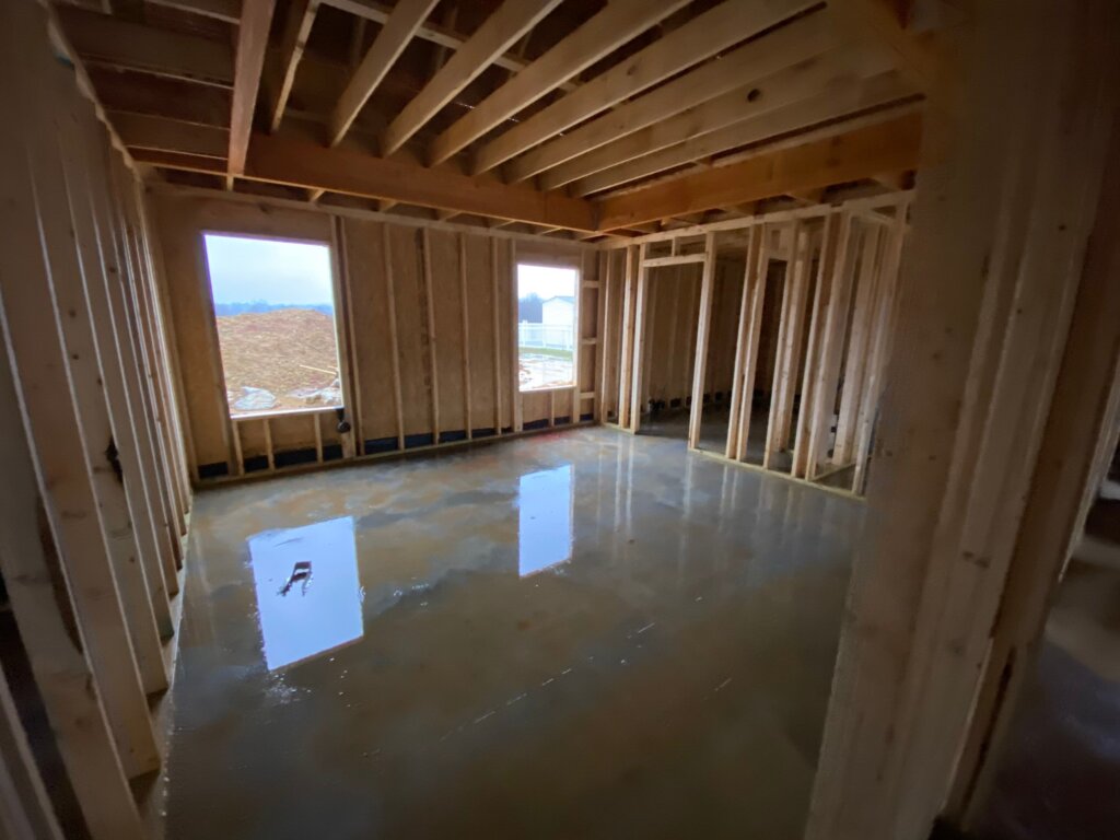 Luxury custom home under construction featuring interior wood framing, exposed ceiling joists, and large windows in Decatur, AL.