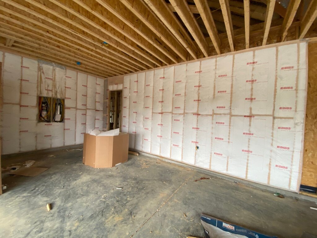 Luxury custom home garage under construction with insulated walls, exposed ceiling joists, and electrical rough-ins in New Market, AL.