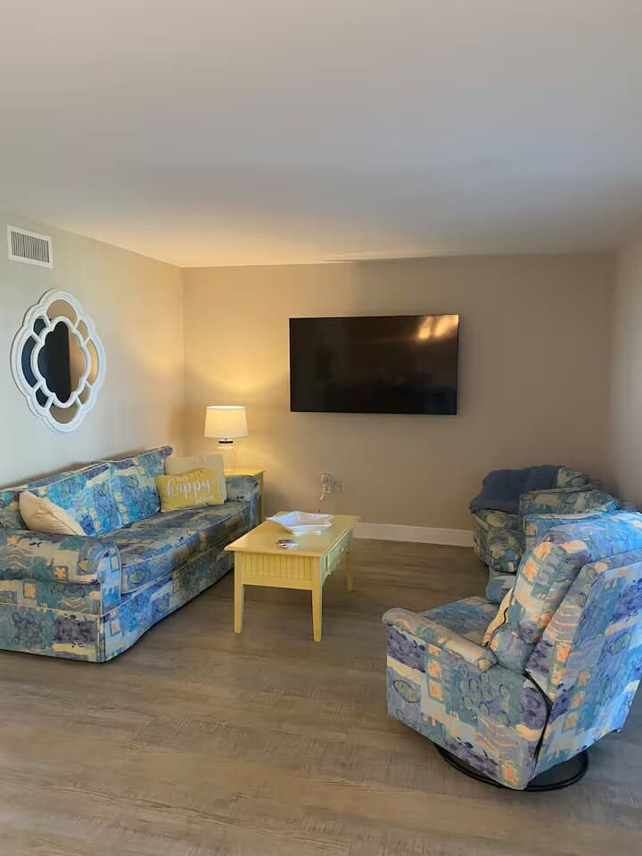 Unit 244 living room with floral sofa and wall-mounted TV