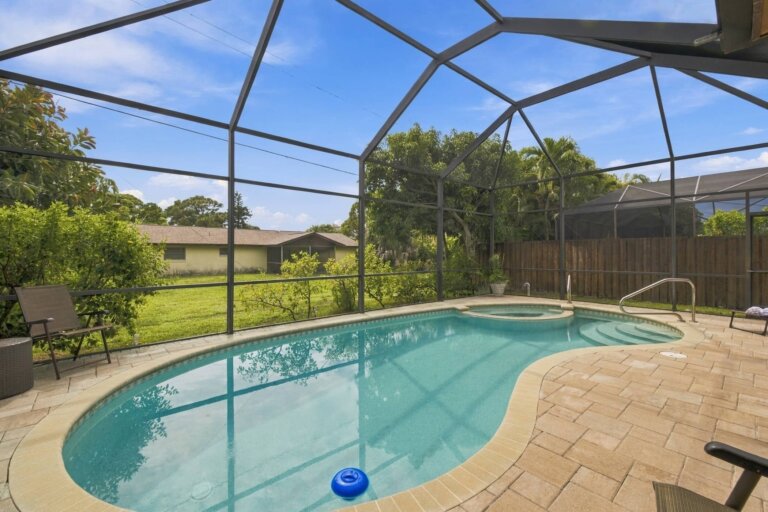 Screened swimming pool overlooking a green lawn and tropical trees
