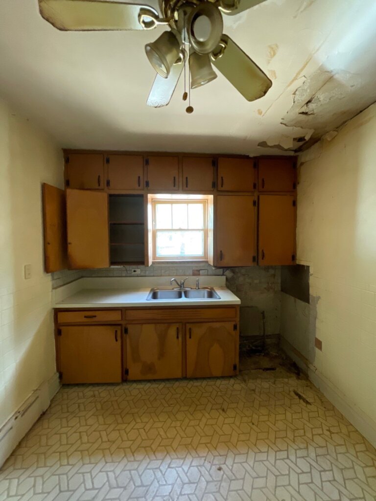 Empty kitchen in a Lake County home with exposed subfloor and ceiling water damage before Greentown Home Buyers purchased it as-is