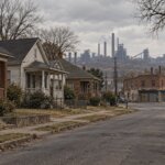 Quiet residential street in Ensley, Birmingham, with older brick houses and an industrial skyline behind