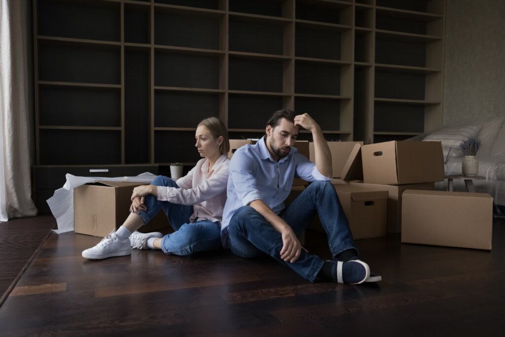 Tired couple sitting on the floor among moving boxes