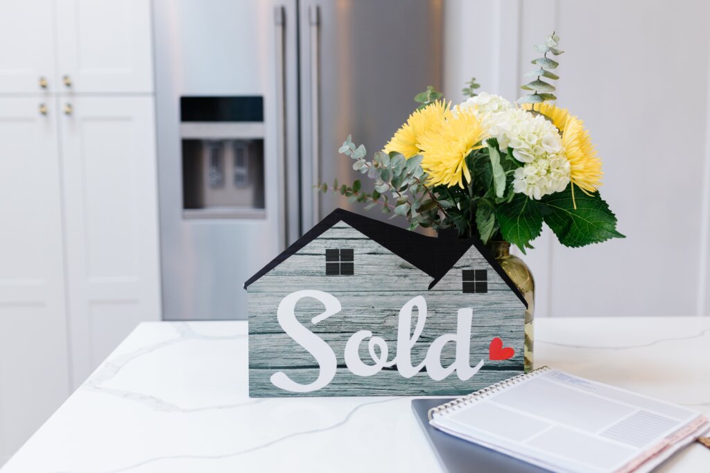 House-shaped Sold sign with flowers on a kitchen counter
