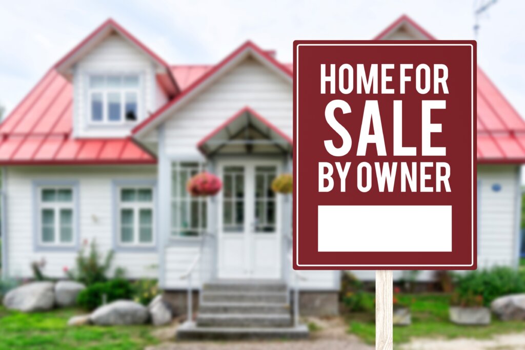White house with a red Home for Sale by Owner sign