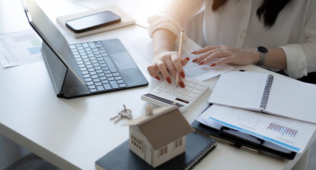 Person working on paperwork at a desk with a laptop and a small house model