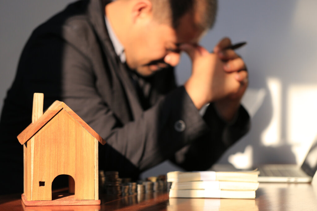 Worried man with his head in his hands beside a small wooden house model