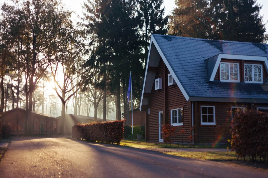 Brick house with a blue roof beside a tree-lined road at sunrise