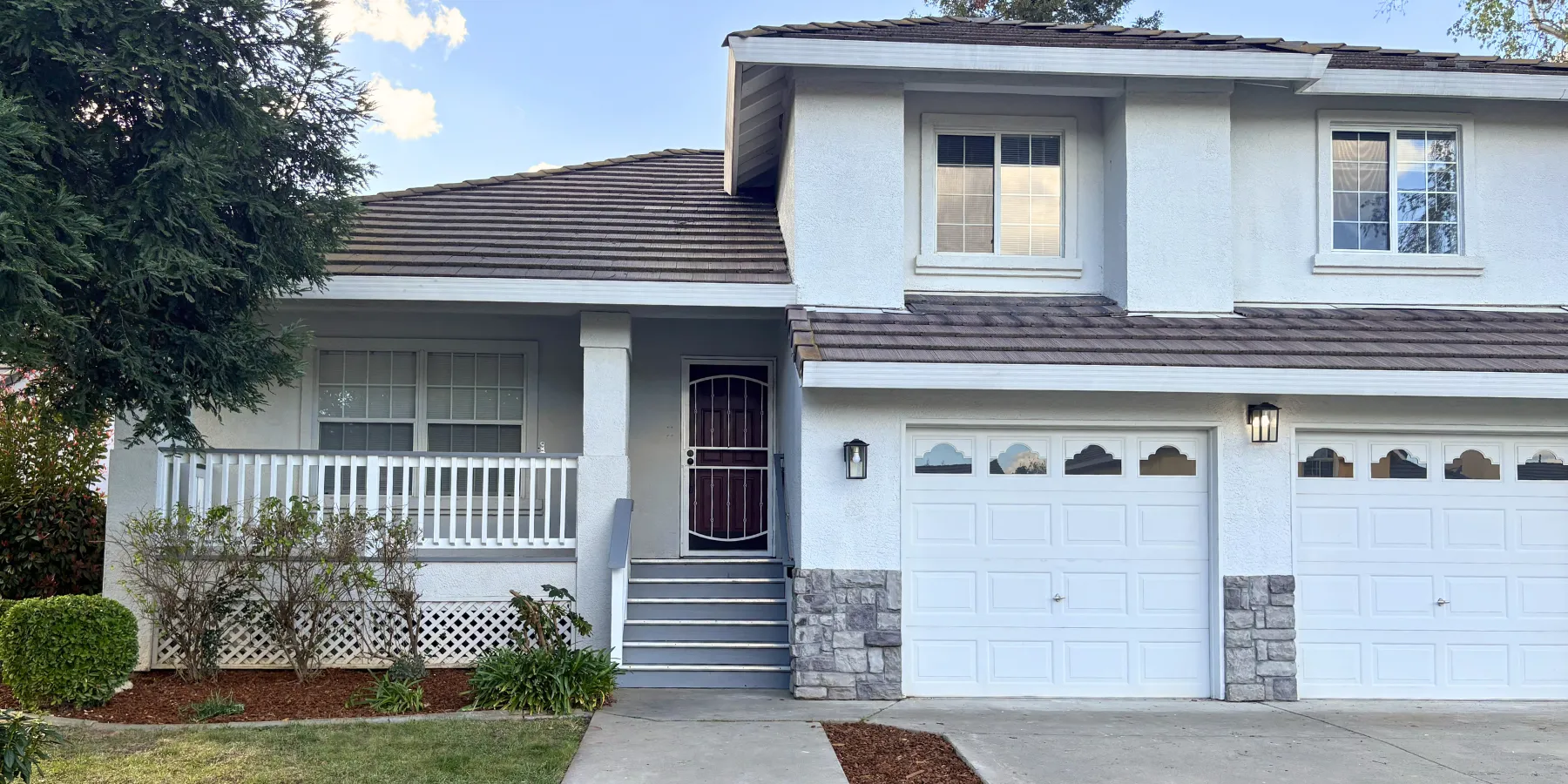 Two-story home with white stucco walls, a covered front porch and a two-car garage