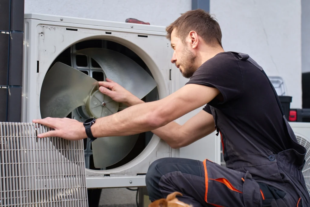 HVAC Technician Inspecting Fan Inside Outdoor Heat Pump Thanks to Local SEO
