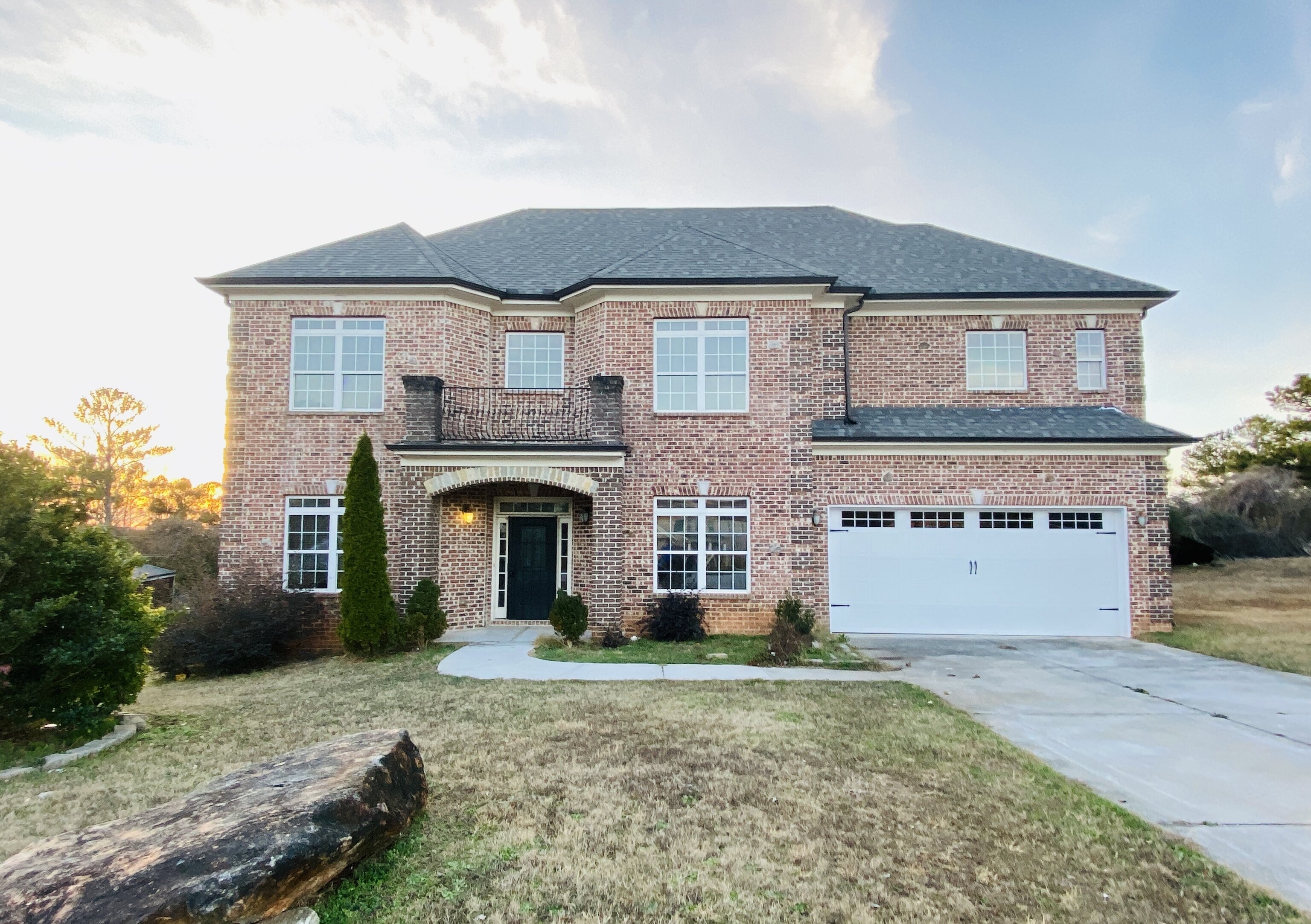 Large two-story red brick house with a two-car garage, a dark front door, and a second-floor balcony.