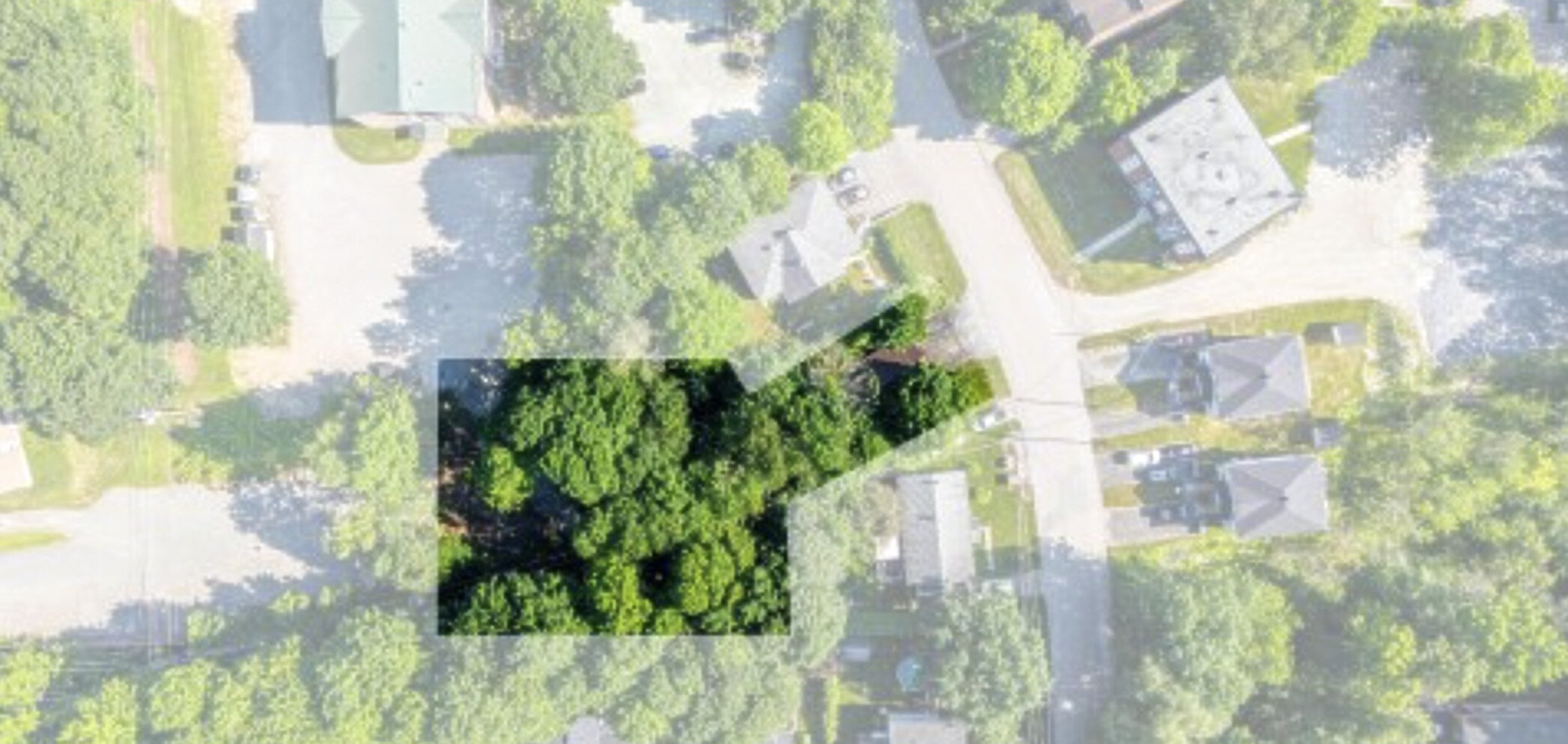 Aerial view of a treed land parcel highlighted for sale