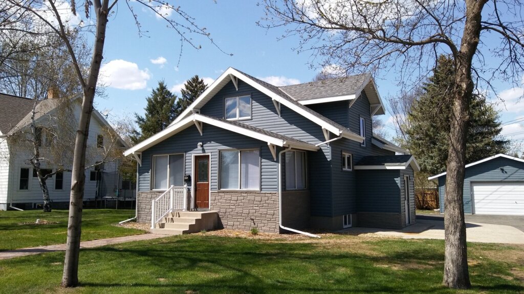 Two-story blue-gray house with front porch, garage, and lawn.